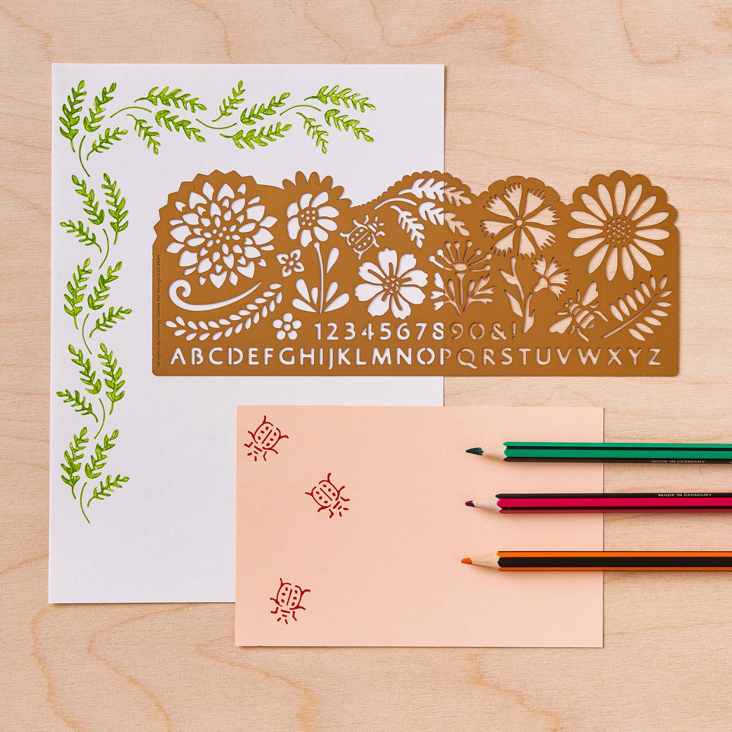Decorative brass Botanical ruler with letter and number designs on a wooden surface with a pencil and paper.