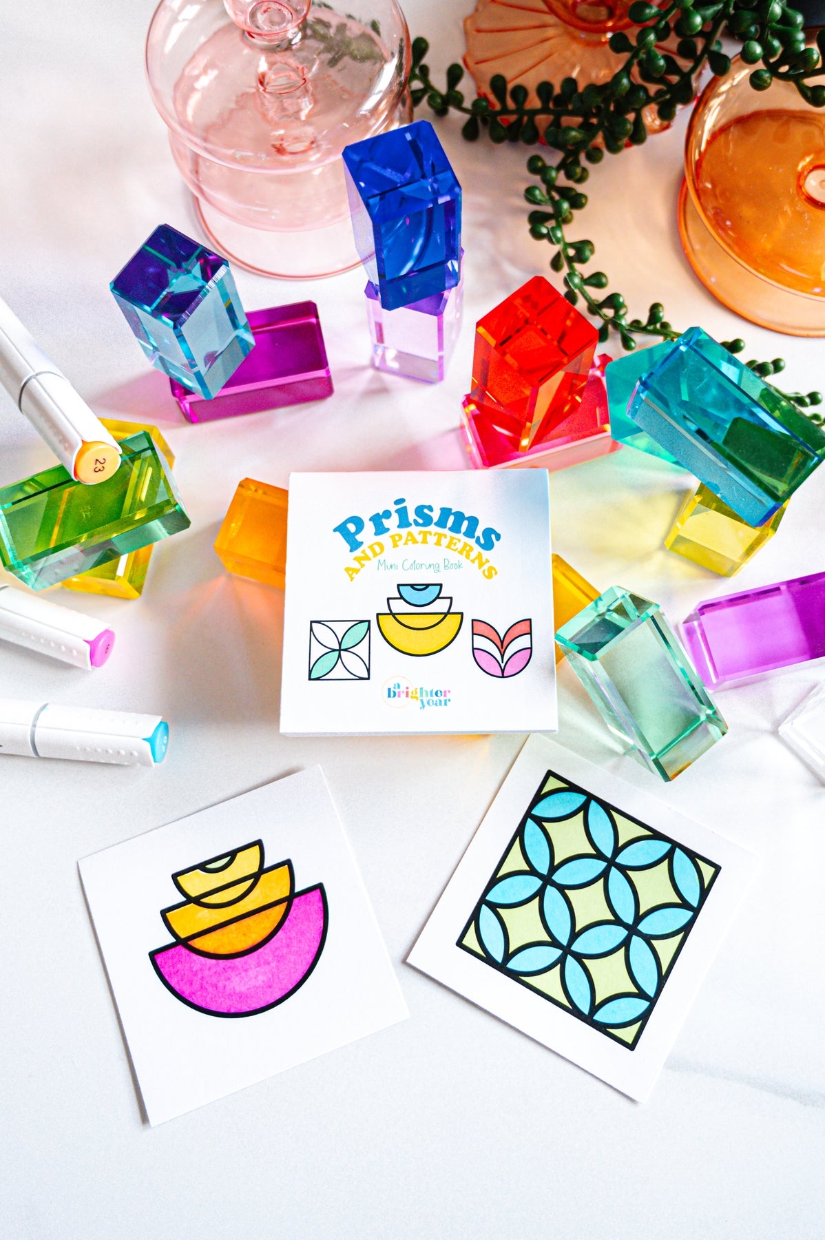 cover of prisms book with two completed pages surrounded by colorful acrylic blocks