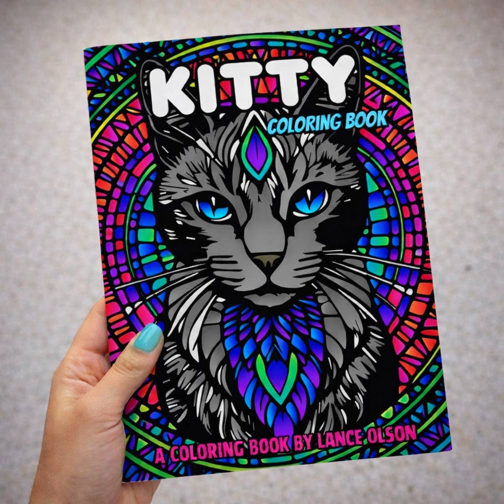 A white hand with blue nail polish holding the Kitty coloring book featuring a blue eyed grey cat with a stylized third eye.