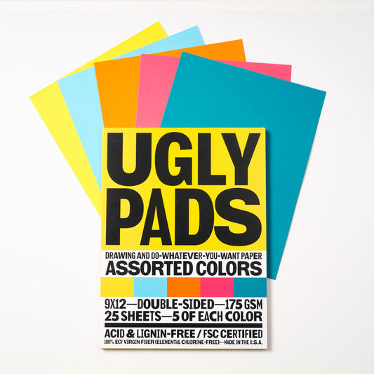 Packaging of "juicebox" Uglypad with single sheets spread around it, in yellow, light blue, orange, coral, and teal