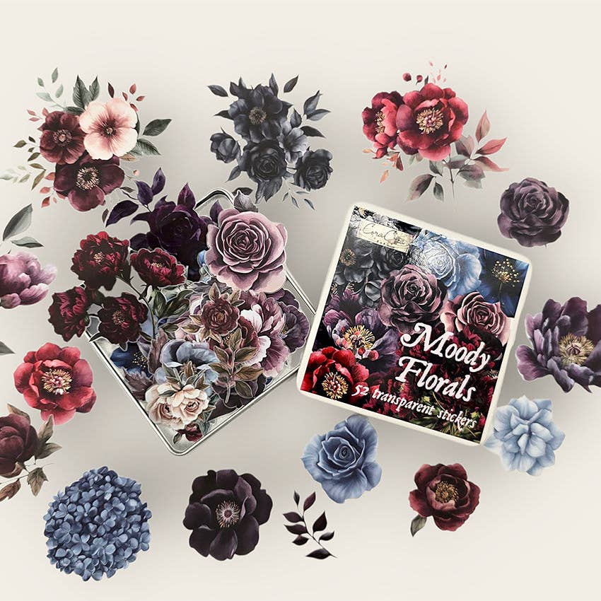 A flat-lay presentation of a floral sticker kit, showing a box labeled 'Moody Florals' and a clear container filled with various watercolor-style floral stickers in dark, muted, and pastel tones on a light cream background.