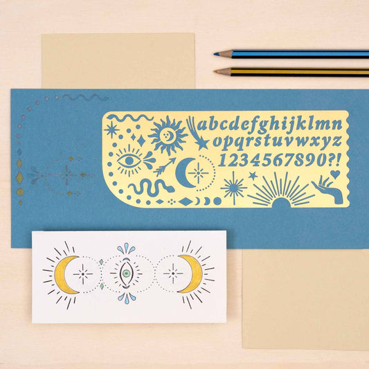 Decorative brass Celestial ruler with letter and number designs on a blue surface with a pencil and paper.