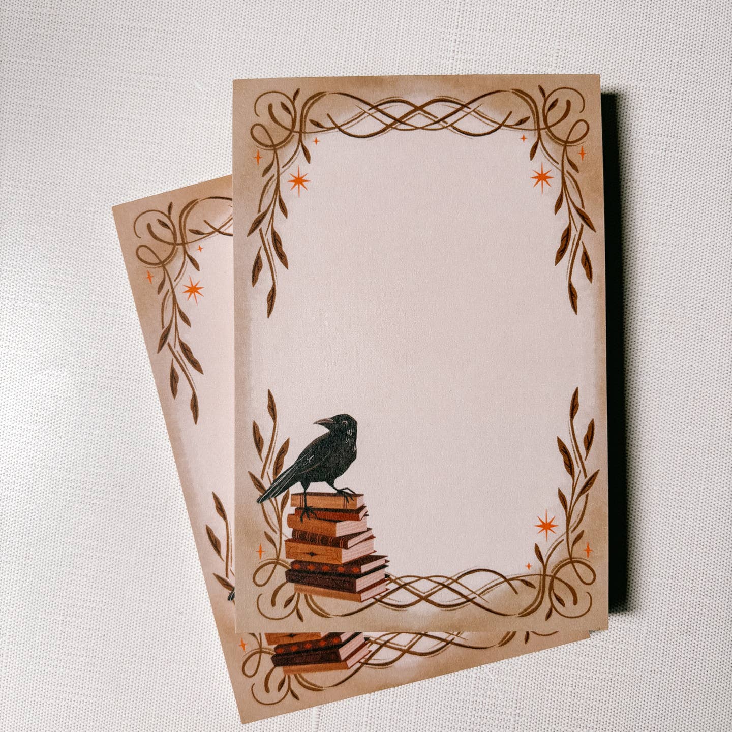 Notepad with a border of flourishes and stars with a crow atop a stack of books in the bottom corner