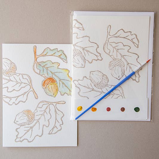 photo of one painted and one unpainted image of the Acorn watercolor card kit with a paintbrush and dot card on a beige background
