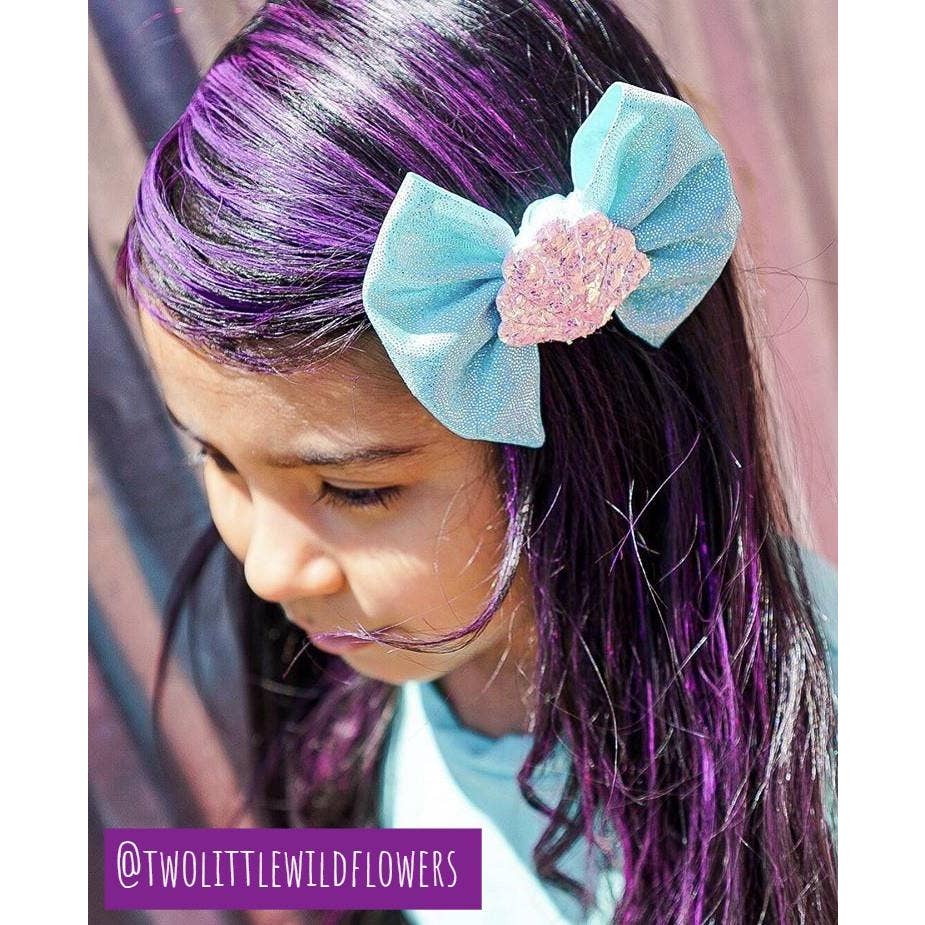 purple hair chalk highlights on the black hair of a young girl with brown skin with a blue bow in her hair
