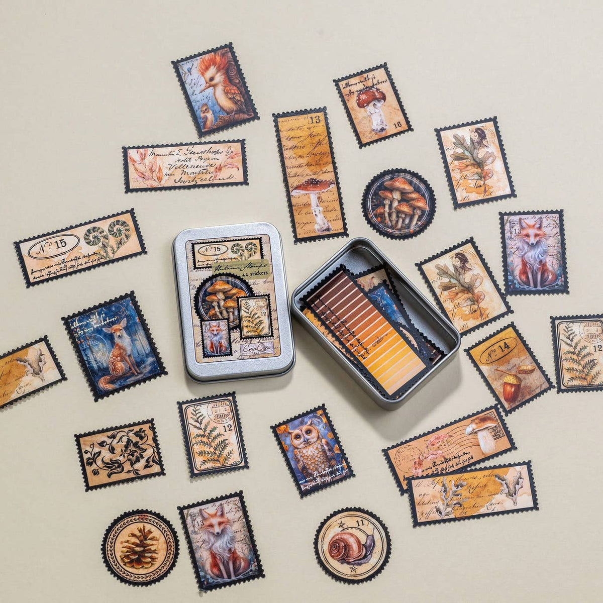 A tin of illustrated forest-themed cards or stickers arranged on a light beige background, with several sample pieces scattered around it. The pieces feature vintage-style designs including foxes, owls, mushrooms, leaves, and text panels in muted blue, brown, tan, and orange tones.