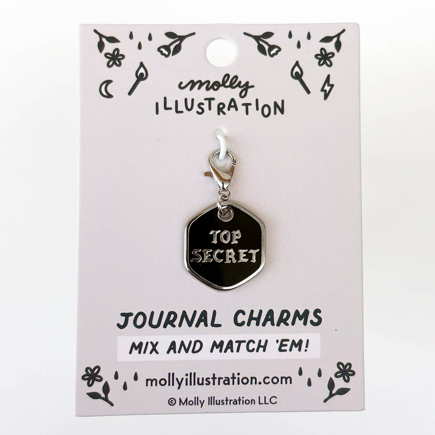 A silver-toned metal journal charm shaped like a hexagonal tag with the words 'TOP SECRET' in raised silver lettering on a black background, attached to a white display card printed with the brand name Molly Illustration.