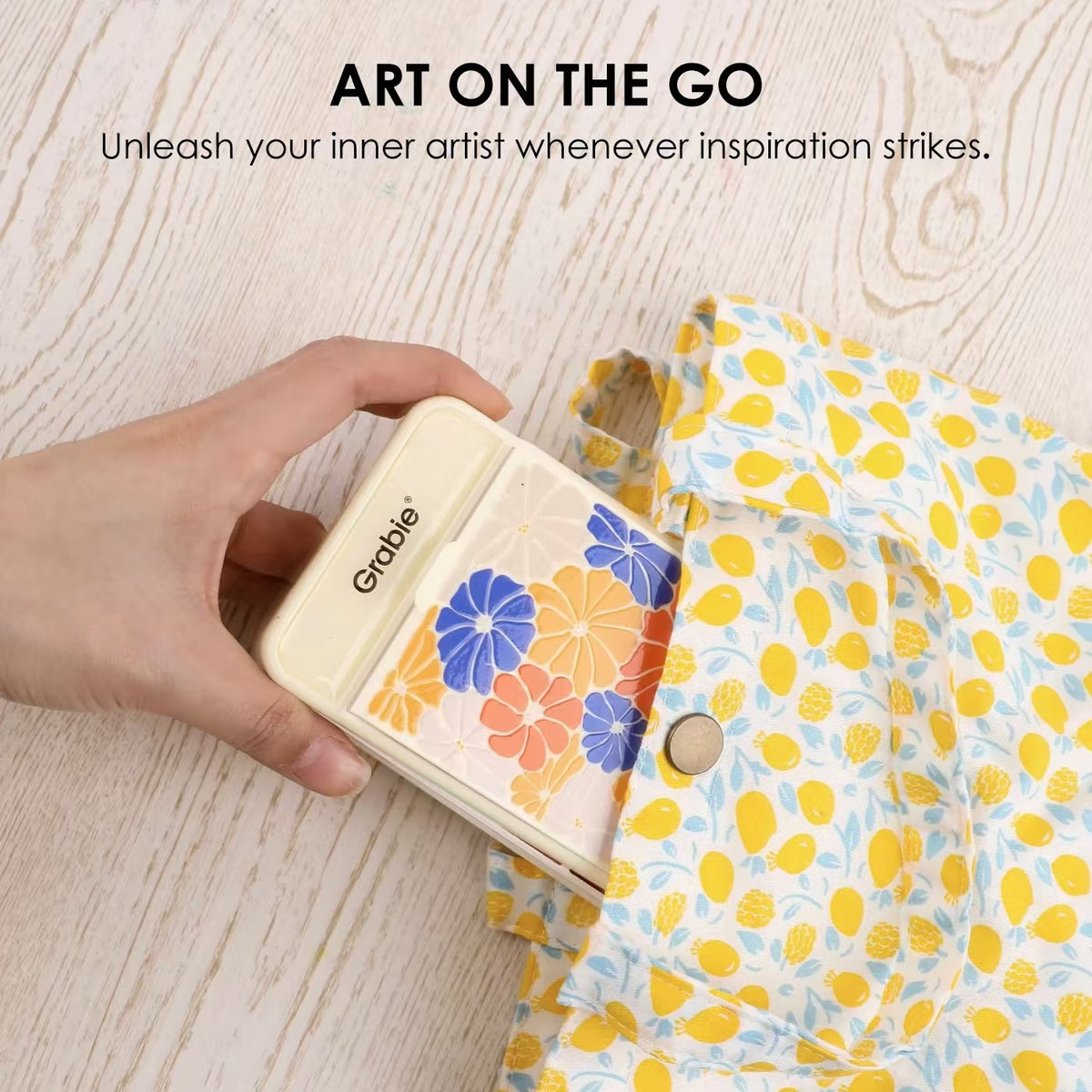 A white hand takes the Grabie Foldable Watercolor Set from a canvas purse with text that reads, "Art on the Go - Unleash your inner artist whenever inspiration strikes"