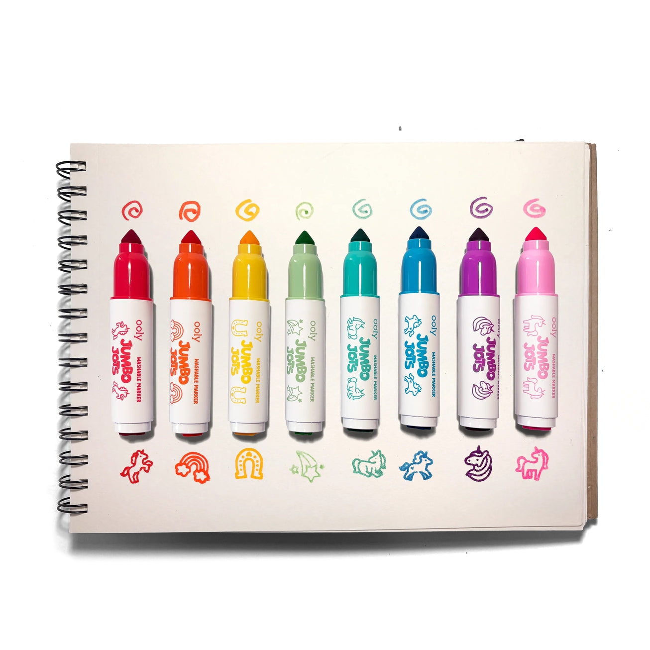 A spiral-bound notebook showing eight colorful jumbo markers arranged horizontally on the cover, each with a small doodle and showing the stamps: red unicorn, orange rainbow, yellow horseshoe, green shooting star, teal unicorn, blue pony, purple unicorn, and pink unicorn
