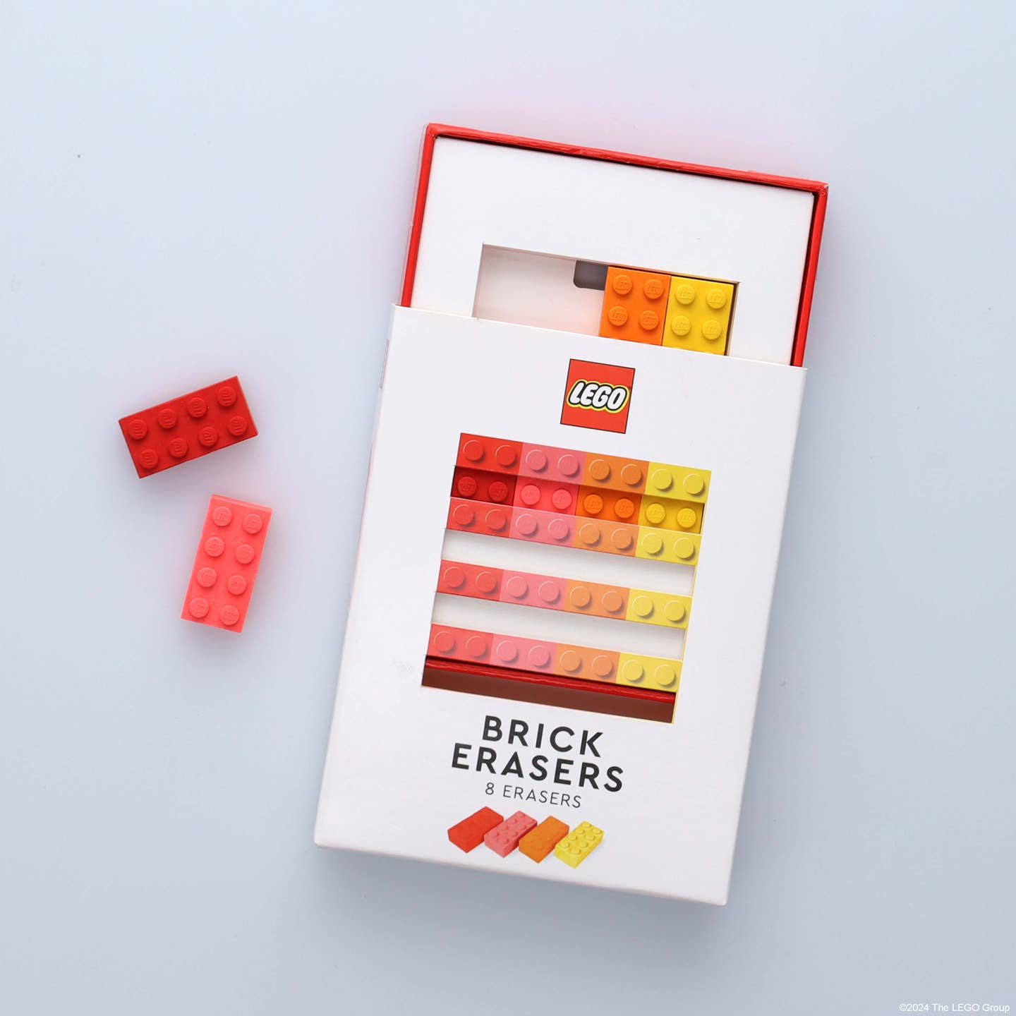 A photo of a partially opened box of Lego Brick Erasers with a red and orange Lego Brick Eraser on a white background