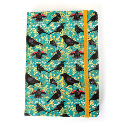 Notebook with blackbirds and crows with a floral pattern on a teal background with a yellow elastic closure strap