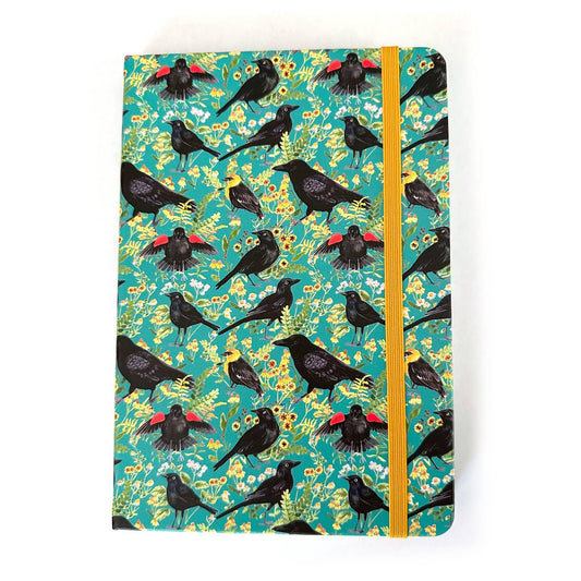 Notebook with blackbirds and crows with a floral pattern on a teal background with a yellow elastic closure strap
