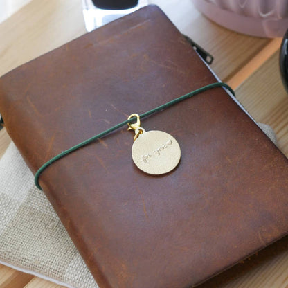 Back of the brass "For You" journal charm engraved with the words, "for you" in a cursive style
