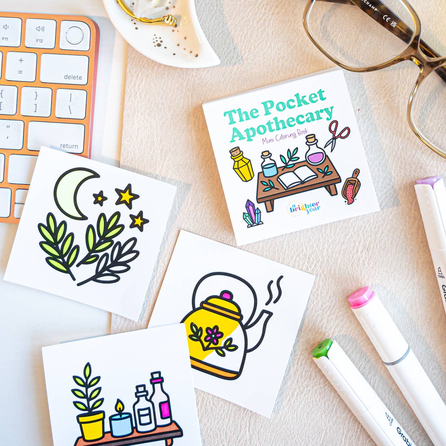 the pocket apothecary book with three pages partially colored in featuring a moon and plants, a flora patterned tea kettle, and a shelf with bottles and books