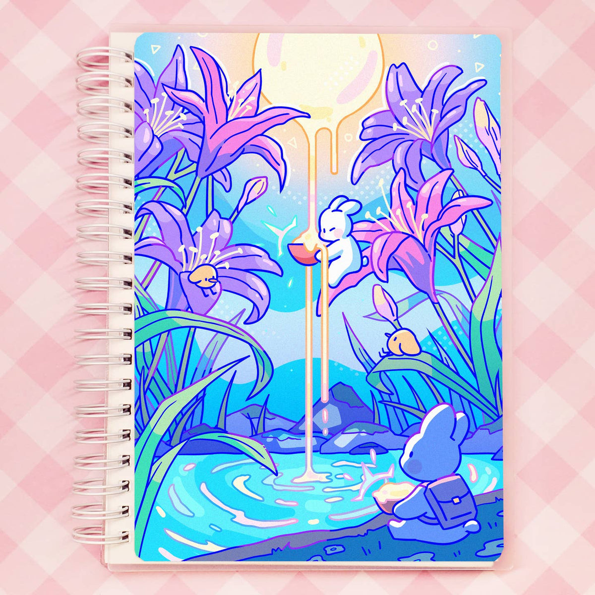 A spiral-bound reusable sticker notebook with a colorful illustrated cover showing purple flowers, a white bunny holding a red cup under a dripping moon, and a blue rabbit by a pond, set against a pink checkered background.