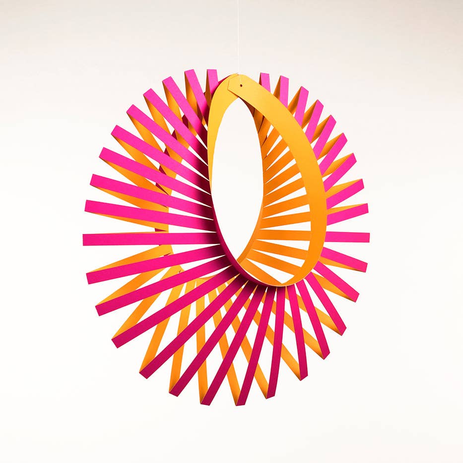 Cadentia 3D Pop Up Paper Mobile in a graphic crescent shape made from pink and orange paper strips on a white background