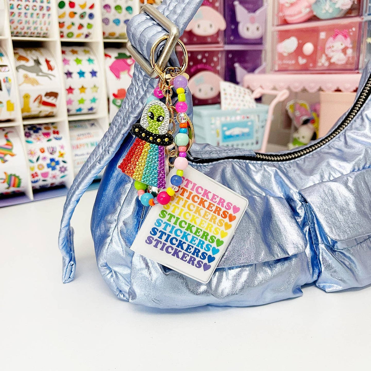 Silver handbag with colorful keychain and 'stickers' tag, set against a colorful store background.
