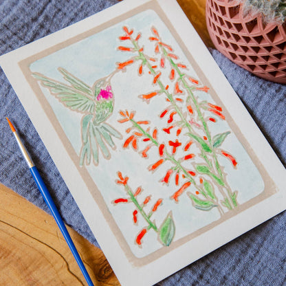 Card with an illustration of penstemon flowers and a ruby throated hummingbird with a paintbrush on a blue and brown background