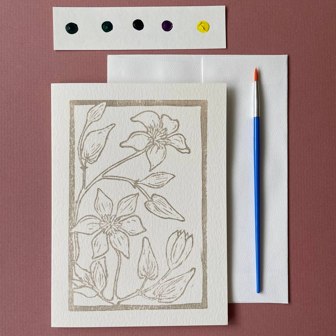 Card with a floral illustration with watercolors and a paintbrush on a brown surface