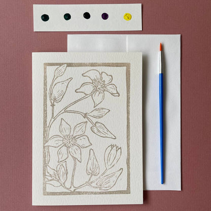 Card with a floral illustration with watercolors and a paintbrush on a brown surface