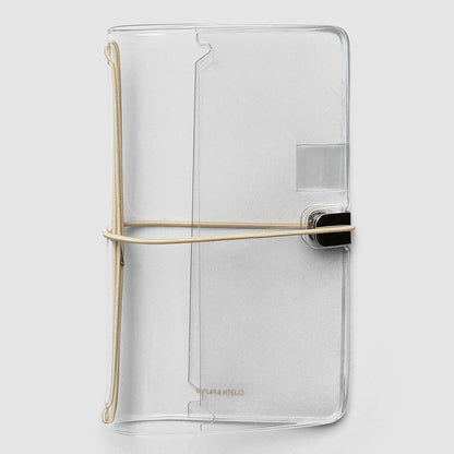 A clear, transparent notebook cover with a minimalist design, featuring a gold-colored elastic band closure and a black metal clasp, shown on a light gray background.