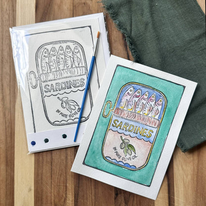 watercolor card kit in plastic sleeve with a paintbrush and a completed sardine painting on a green background