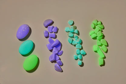 a glow stone in each of three colors, purple, blue, and green next to piles of multicolor glow pebbles