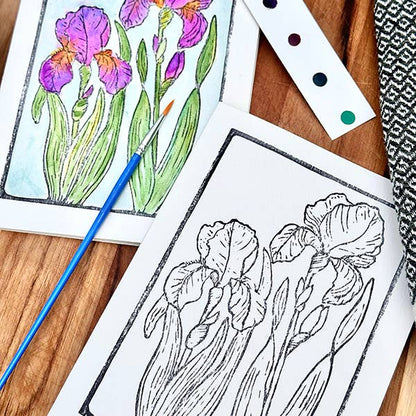 Card with an illustration of irises with watercolors and a paintbrush on a wooden surface