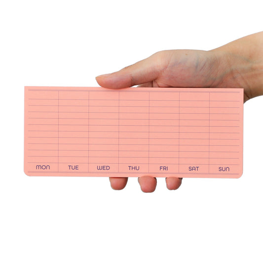 A white skinned hand holding a pink weekly planner sticky note pad with days of the week on a white background
