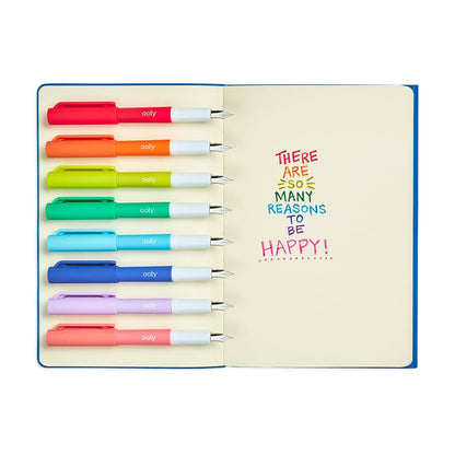 Ooly Color Write fountain pens, uncapped, showing text written with each on an open notebook; each word in a different color that reads, "There are so many reasons to be happy"