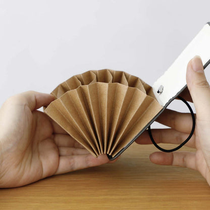 two white hands holding open the Hightide card sized accordion file over a wooden surface