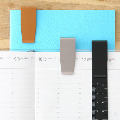 Hightide's Clip Ruler shown in black clipped to an open planner on a wooden background
