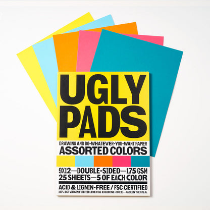 Packaging of "juicebox" Uglypad with single sheets spread around it, in yellow, light blue, orange, coral, and teal